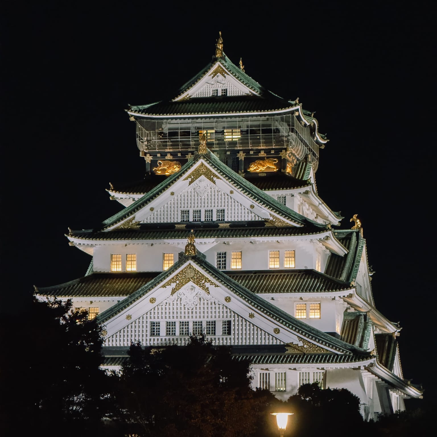 The historic Osaka Castle in Japan, brightly illuminated against the night sky with intricate gold detailing visible.